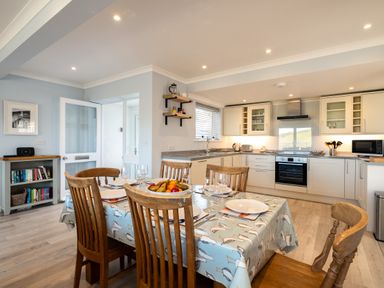 A kitchen and dining area with wooden chairs and a table covered with a bird-patterned tablecloth at Harbour Lights Port Isaac