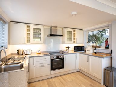A kitchen with white cabinets stainless steel sink electric oven microwave and countertop appliances at Harbour Lights Port Isaac