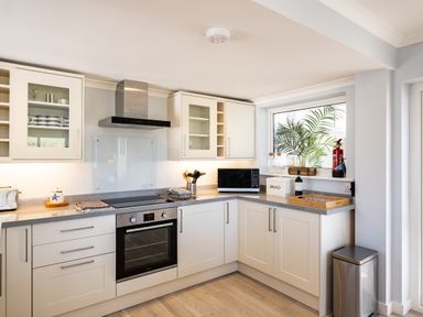 A kitchen with white cabinets a built in oven a microwave a potted plant and kitchen utensils at Harbour Lights Port Isaac