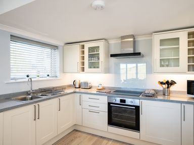 A kitchen with white cabinets and grey countertops with a sink oven and small plants at Harbour Lights Port Isaac