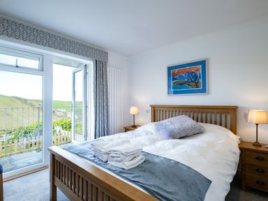 A bedroom with a wooden bed frame bedside tables lamps and a glass door leading to a balcony at Harbour Lights Port Isaac