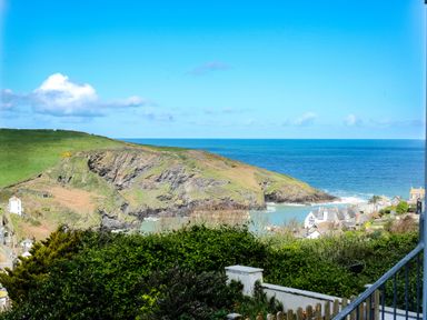A coastal view with a rocky hillside green grass and houses near the sea at Harbour Lights Port Isaac
