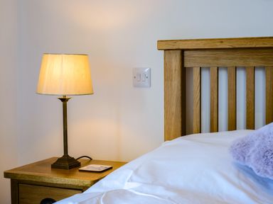 A bedside table with a lamp and a coaster next to a wooden bed frame at Harbour Lights Port Isaac