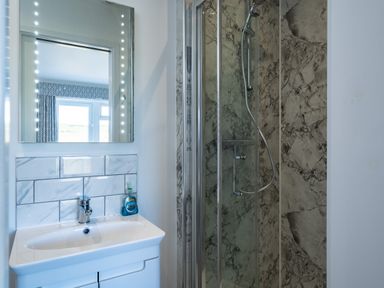 A bathroom with a sink and mirror beside a shower with marble walls at Harbour Lights Port Isaac