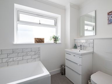 A bathroom with a bathtub a vanity with sink and mirror a window with a plant and wooden decoration at Harbour Lights Port Isaac