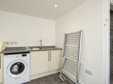 A utility room with a washing machine, sink, drying rack, and storage cabinets at Harbour Lights Port Isaac
