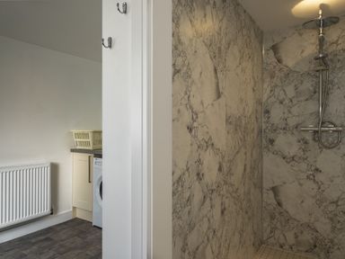 A laundry area with a washing machine and basket next to a shower with marble walls at Harbour Lights Port Isaac