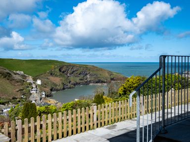 A coastal view with a wooden fence and metal railing overlooking a bay and houses at Harbour Lights Port Isaac