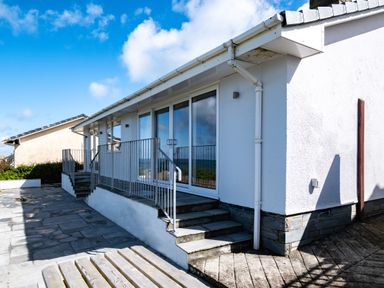 An exterior view of a white building with stone steps and metal railings under a blue sky at Harbour Lights Port Isaac