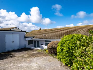 Exterior of a single-story building with a sloped roof and a concrete driveway with bushes in front at Harbour Lights Port Isaac