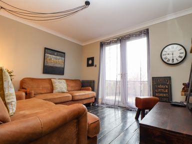 A living room with brown leather sofas a wall clock and a sign near glass doors at Hillcroft in St Austell