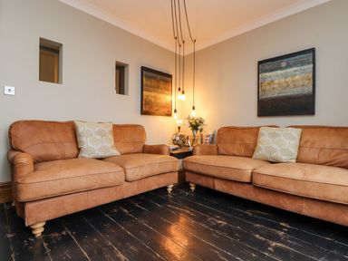 A living room with two brown leather sofas a side table with flowers and hanging lights at Hillcroft in St Austell