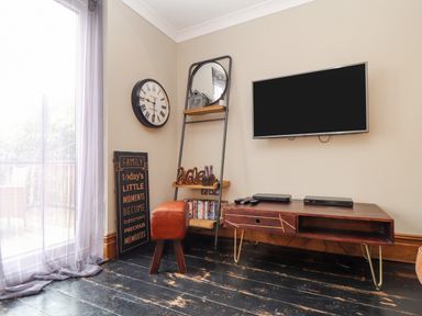 A corner of a living room with a wall clock mirror wooden shelves small stool and a wall mounted television at Hillcroft in St Austell