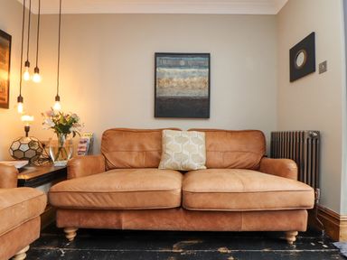 A living room with a brown leather sofa a side table with flowers and hanging lights at Hillcroft in St Austell