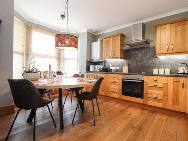 A kitchen with wooden cabinets dining table black chairs and large windows at Hillcroft in St Austell
