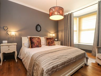 A bedroom with a double bed two bedside tables lamps and large windows with curtains at Hillcroft in St Austell