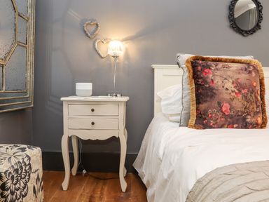 A bedroom with a bed, nightstand with lamp and speaker, decorative hearts on wall at Hillcroft in St Austell