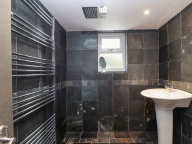 A bathroom with black tiled walls and floor a white pedestal sink a towel rack and a small window at Hillcroft in St Austell