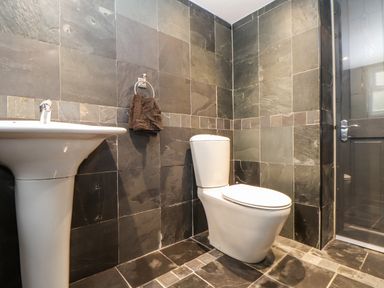 A bathroom with a white toilet pedestal sink and dark tiled walls and floor at Hillcroft in St Austell