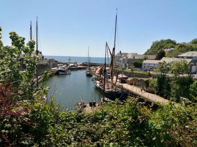 A harbor with sailboats docked along a walkway and buildings nearby at Hillcroft in St Austell