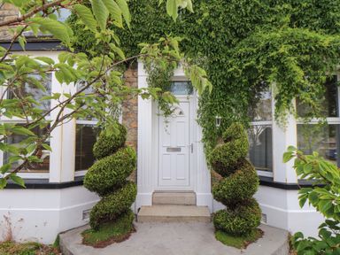 A front door with spiral shaped bushes on each side and climbing plants around an entrance at Hillcroft in St Austell
