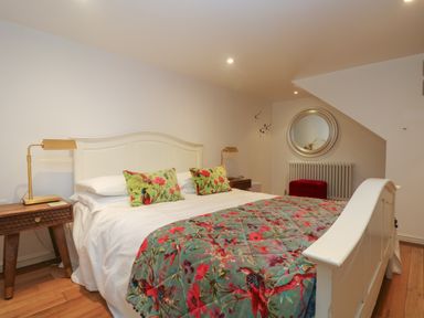 A bedroom with a white bed frame floral bedding wooden side tables and a round mirror on the wall at Hillcroft in St Austell