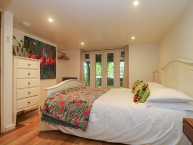 A bedroom with a bed with floral bedding a white dresser and a painting of flamingos at Hillcroft in St Austell