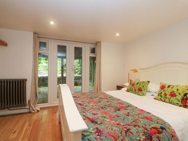 A bedroom with a bed covered with a floral patterned blanket and pillows by glass doors at Hillcroft in St Austell