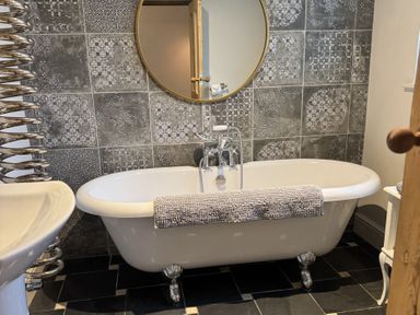 A bathroom with a clawfoot bathtub a round mirror and patterned wall tiles at Hillcroft in St Austell