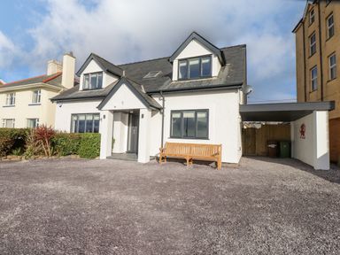 A white two-story house with a porch and bench in front at Tarth Y Mor in Criccieth