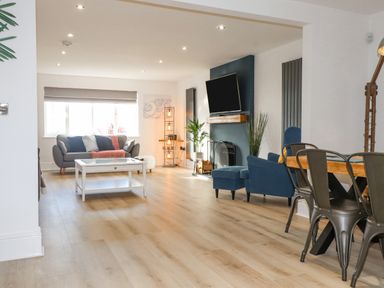 A living room with a gray sofa a white coffee table a blue armchair a fireplace and a dining table with metal chairs at Tarth Y Mor in Criccieth