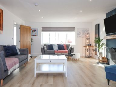A living room with grey sofas a white coffee table and a fireplace at Tarth Y Mor in Criccieth