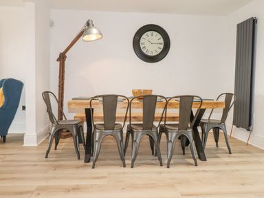 A dining area with a wooden table metal chairs a large wall clock and a floor lamp at Tarth Y Mor in Criccieth