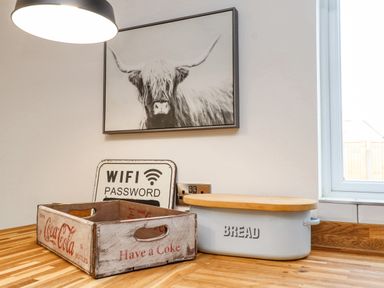 A kitchen counter with a Coca Cola wooden crate a bread bin a sign with wifi password and a framed picture of a highland cow at Tarth Y Mor in Criccieth
