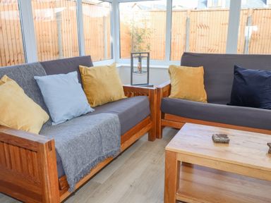 A sunroom with wooden framed sofas with cushions and a wooden coffee table at Tarth Y Mor in Criccieth