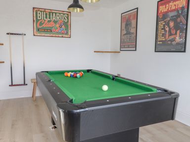 A room with a pool table two pool cues on the wall and framed posters at Tarth Y Mor in Criccieth