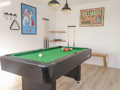 A billiards room with a pool table cues on the wall a bench and two posters at Tarth Y Mor in Criccieth