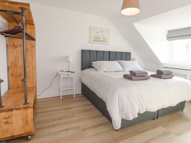 A bedroom with a double bed bedside tables lamps and a wooden open wardrobe at Tarth Y Mor in Criccieth