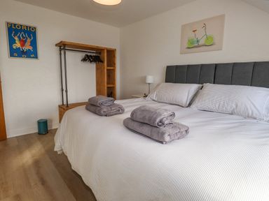 A bedroom with a double bed with gray headboard and folded towels on top at Tarth Y Mor in Criccieth