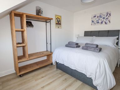 A bedroom with a double bed and wooden open wardrobe with hangers at Tarth Y Mor in Criccieth