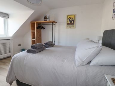 A bedroom with a bed and folded towels on it a wooden open wardrobe and a window at Tarth Y Mor in Criccieth