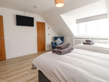 A bedroom with two single beds with towels on them a blue armchair wooden doors and a wall-mounted TV at Tarth Y Mor in Criccieth