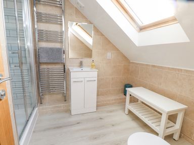 A bathroom with a shower, white sink cabinet, mirror, towel rack, bench, and skylight at Tarth Y Mor in Criccieth