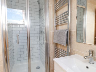 A bathroom with a shower enclosure tiled with white subway tiles a chrome towel rail with a gray towel and a white sink with a chrome faucet at Tarth Y Mor in Criccieth