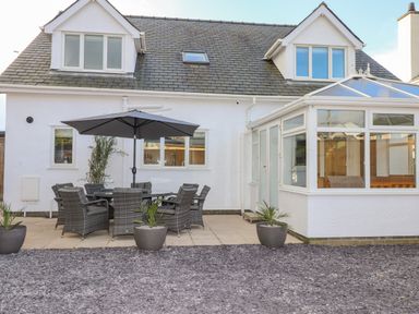 An outdoor patio area with a table and chairs under an umbrella beside a conservatory at Tarth Y Mor in Criccieth