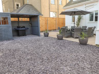 A backyard patio area with a covered barbecue grill and outdoor dining table with umbrella at Tarth Y Mor in Criccieth