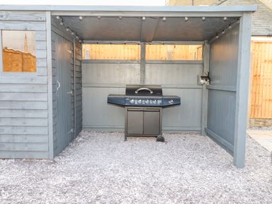 A covered outdoor area with a gas grill and string lights on the ceiling at Tarth Y Mor in Criccieth