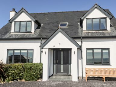 A white house with a black roof black framed windows a black front door and a wooden bench outside at Tarth Y Mor in Criccieth
