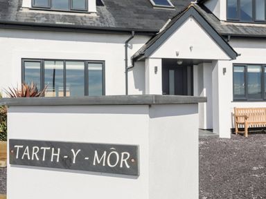 The exterior of a white house with a slate roof and a sign that reads Tarth Y Mor near the entrance at Tarth Y Mor in Criccieth