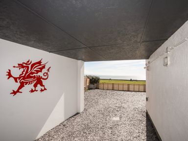 A covered outdoor area with a red dragon wall decoration and a view of a grassy area and water at Tarth Y Mor in Criccieth